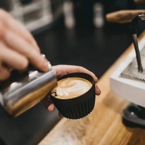 The person is holding the huskee coffee cup with one hand and the pitcher with the other